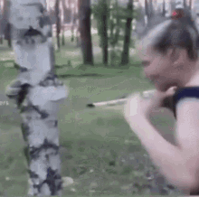 a woman is standing next to a tree in a park holding a sword .