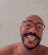 a bald man with a beard and glasses is smiling and waving at the camera .