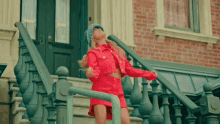 a woman in a red dress is standing on a set of stairs in front of a brick building