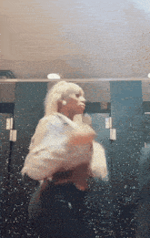 a woman with blonde hair is standing in a bathroom stall