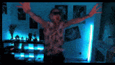 a man with his arms outstretched in a room with blue lights and posters on the wall
