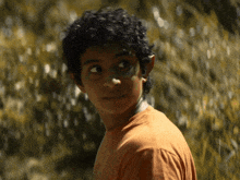 a young man with curly hair is wearing an orange shirt that says ' california ' on it