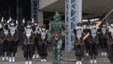 a man in a green costume stands in front of a group of people wearing masks and holding weapons
