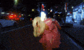 a woman in a pink coat is walking down the street at night