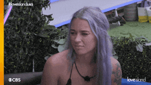 a woman with purple hair is sitting on a couch in front of a cbs logo