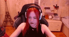 a woman with red hair is wearing headphones and a microphone while sitting in a gaming chair .