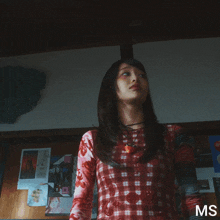 a woman in a plaid shirt is standing in front of a wall with ms written in the corner