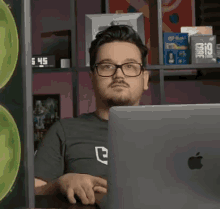 a man with glasses is sitting in front of an apple laptop .