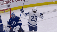 a hockey player wearing a number 23 jersey holds up his stick