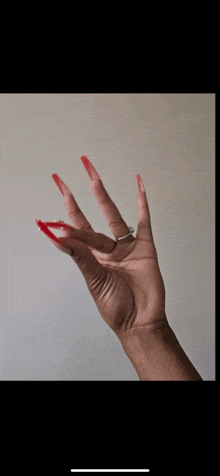 a woman 's hand with long red nails and a ring on it