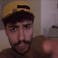 a man with a mustache wearing a yellow hat is pointing his finger at the camera .