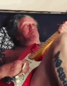 a man is laying on a couch playing a guitar .