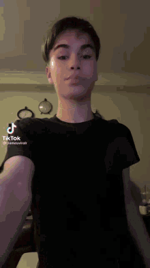 a young man wearing a black t-shirt is taking a selfie with a tiktok app on his phone .