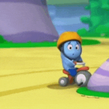 a blue cartoon character wearing an orange helmet is riding a tricycle on a yellow road