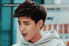 a young man with short hair is wearing a gray hoodie and making a funny face .