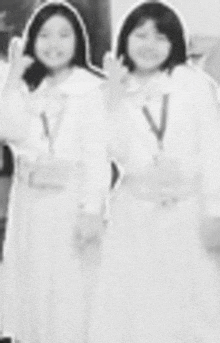 two girls in white dresses are standing next to each other and giving the peace sign .