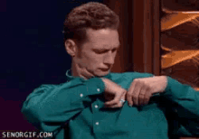 a man in a green shirt is adjusting his shirt sleeves