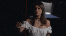a woman in a white off the shoulder dress is standing in a dark room holding a red string .