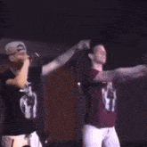 two men are standing next to each other on a stage and one of them is wearing a shirt that says 2pac .
