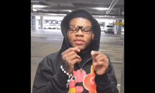 a man wearing glasses and a black hoodie is making a heart with his hands in a parking garage