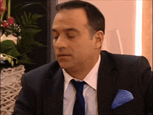a man in a suit and tie is sitting in front of a vase of flowers