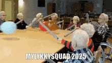 a group of elderly people are sitting around a table with balloons and sticks and the words mylkysquad 2025