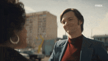 a man in a suit smiles while talking to a woman in front of a max logo