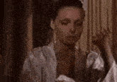 a woman in a robe is standing in front of a window and looking down .