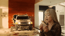 a woman eating a sandwich in front of a car that has a hole in the wall