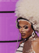 a woman wearing headphones and a large afro wig is standing in front of a purple background ..