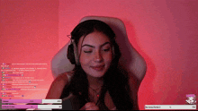 a woman wearing headphones is sitting in a chair with a pink background