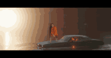 a woman in an orange shirt is standing on top of a car