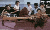 a group of children are gathered around a man laying on a bed with a radio