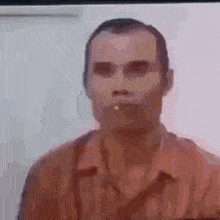 a man in a red shirt is smoking a cigarette in a blurry photo .