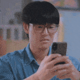 a young man wearing glasses is looking at his cell phone