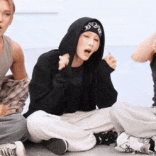 a person wearing a black hoodie with a bandana on their head is sitting on the floor