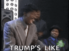 a man in a suit is laughing and saying `` trump 's like '' .