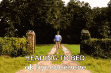 a man is walking down a dirt road with the words heading to bed ok byeeeeeee written on it .