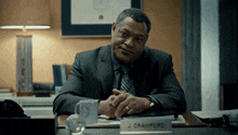 a man in a suit sits at a desk with a name plate that says j. crawford
