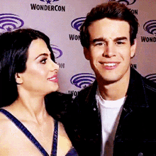 a man and a woman are posing for a picture in front of a wall that says wondercon