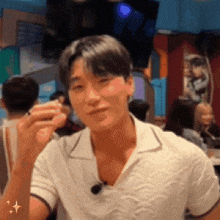a man in a white shirt is sitting at a table in a crowded room holding a glass .