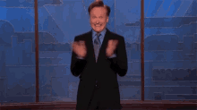 a man in a suit and tie is standing in front of a window and clapping .