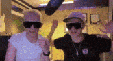 two people wearing sunglasses and hats are standing next to each other in a room .