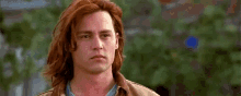 a man with long red hair is wearing a brown jacket and blue shirt .