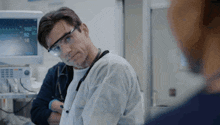 a doctor wearing goggles and a white coat is talking to a nurse .