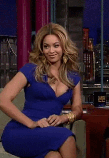 a woman in a blue dress laughs while sitting in front of a tonight show mug