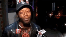 a man wearing a hat and a t-shirt with the number 8 on it is talking into a microphone