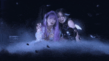 two women are standing next to each other in a dark room . one of the women has purple hair and the other has black hair .