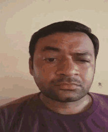 a man with a beard is making a funny face while wearing a purple shirt .