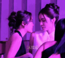 two women are standing next to each other and looking at each other in a room with purple lights .